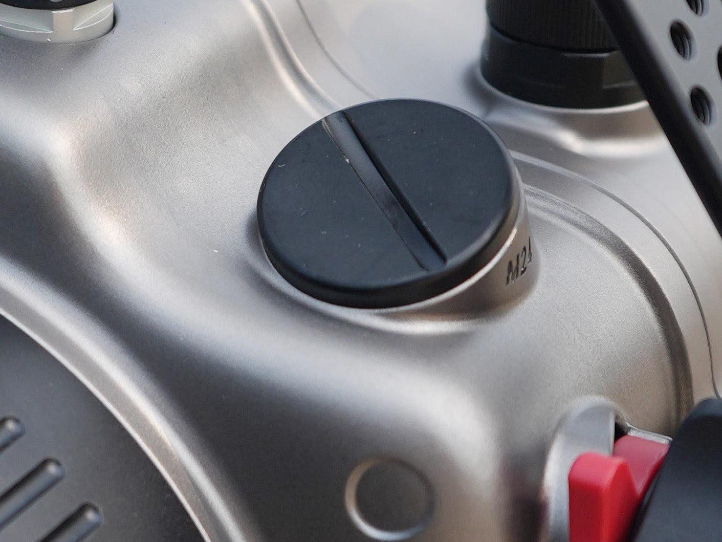 Close-up of a metallic silver machine body with a black circular cap and a small red switch, showing part of the product in detail.
