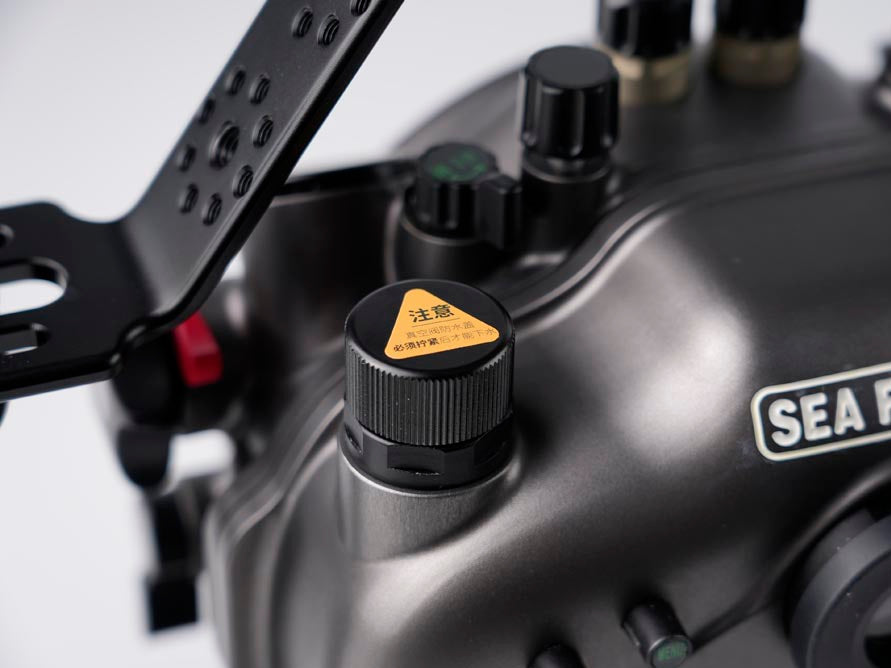 Close-up of a matte black Sea Frog camera housing with a textured black control knob featuring a yellow warning sticker, and part of a black mounting bracket visible on the left.