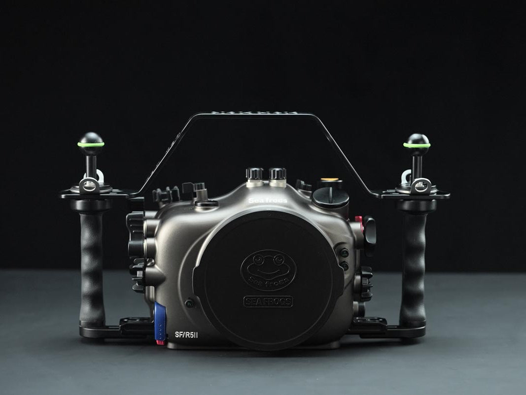 A black and dark gray underwater camera housing with integrated handles and top handle bar, shown from the front against a dark studio background.