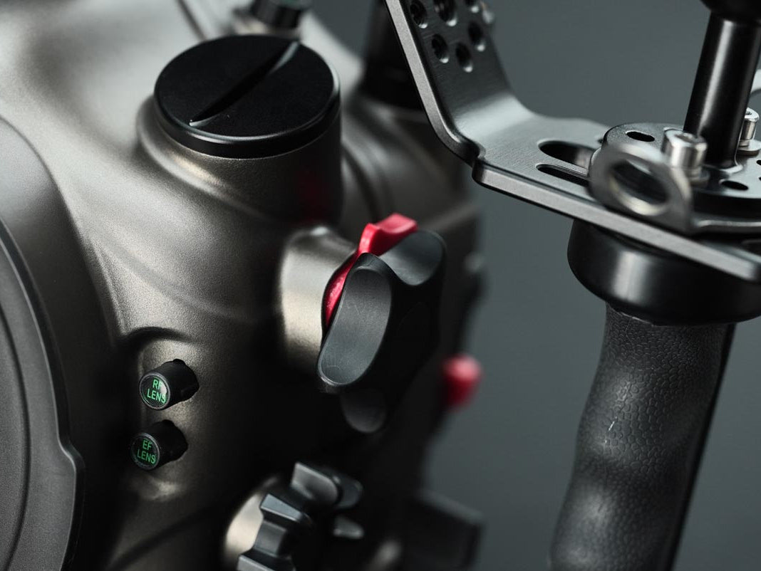 Close-up of a camera body with a metal cage attachment and a black handle, showing control buttons and a red accent on a dark gray background.