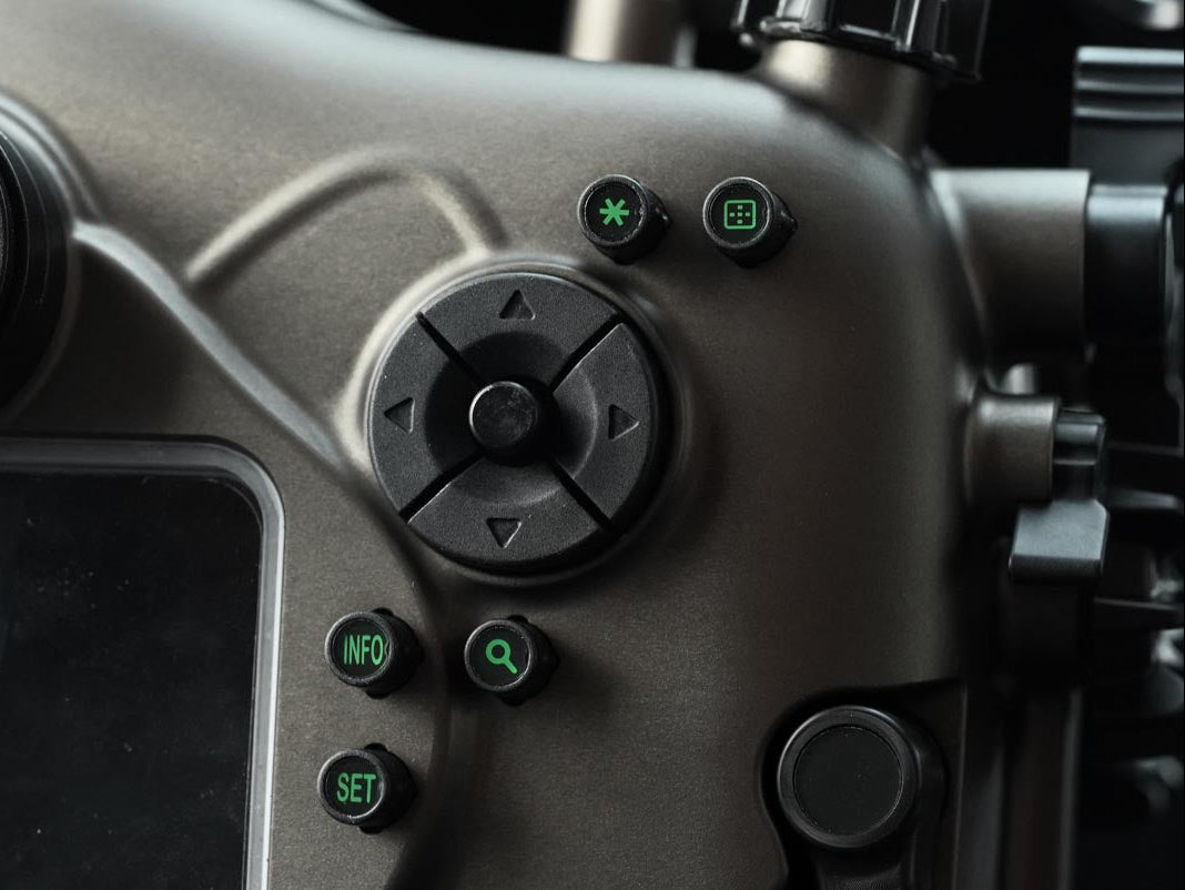 Close-up of a matte dark gray drone remote control showing the directional pad, green power and mode buttons, and a screen edge.
