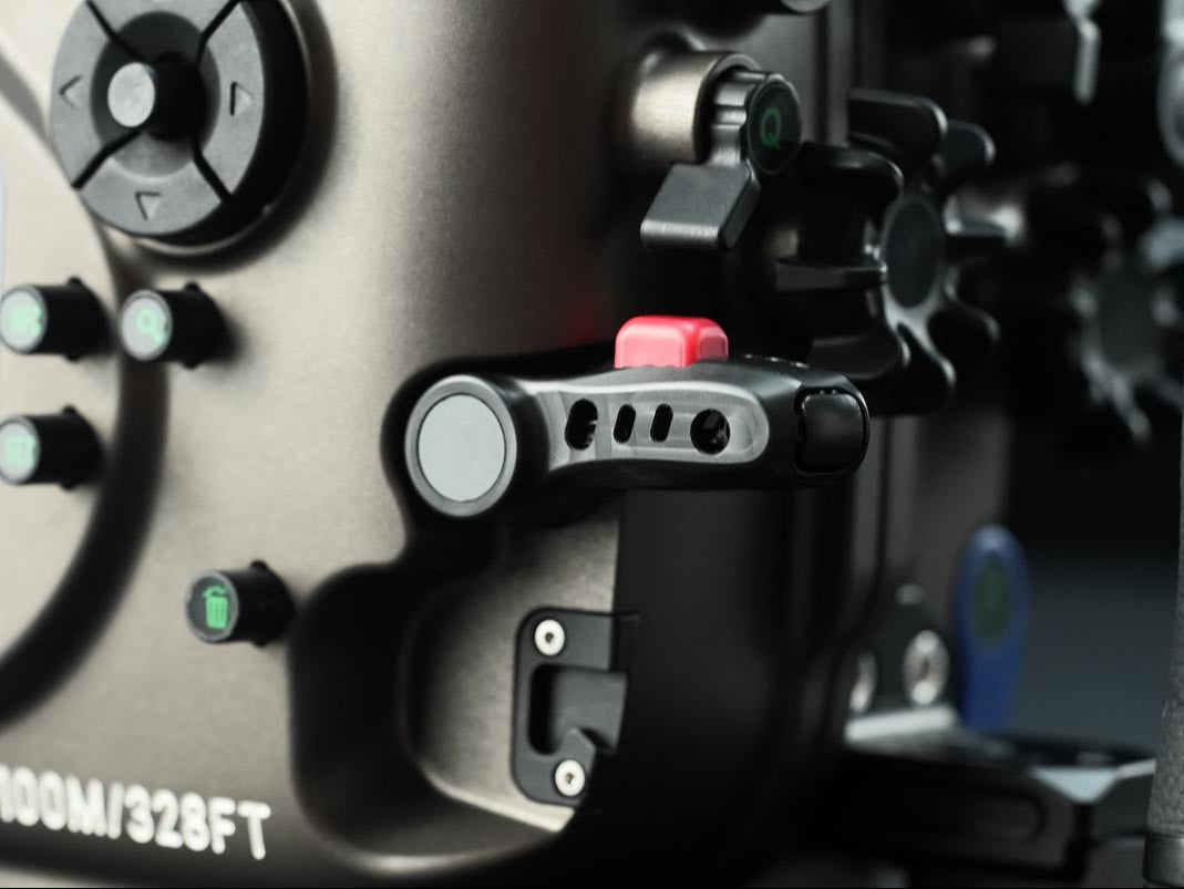 Close-up of a camera rig or monitor housing with black controls, knobs, and a small red switch, showing part of the text '100M/328FT' on a dark metallic surface.